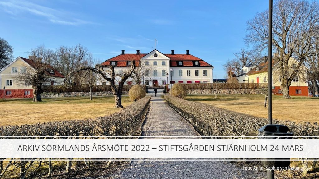 Ett stort ljusfärgat hus med flyglar mot blå himmel och trädgård i tidig vårskrud.